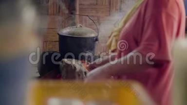 在亚细亚村，一个女人用扇子吹火，一边在篝火上做饭。 女人做传统晚餐